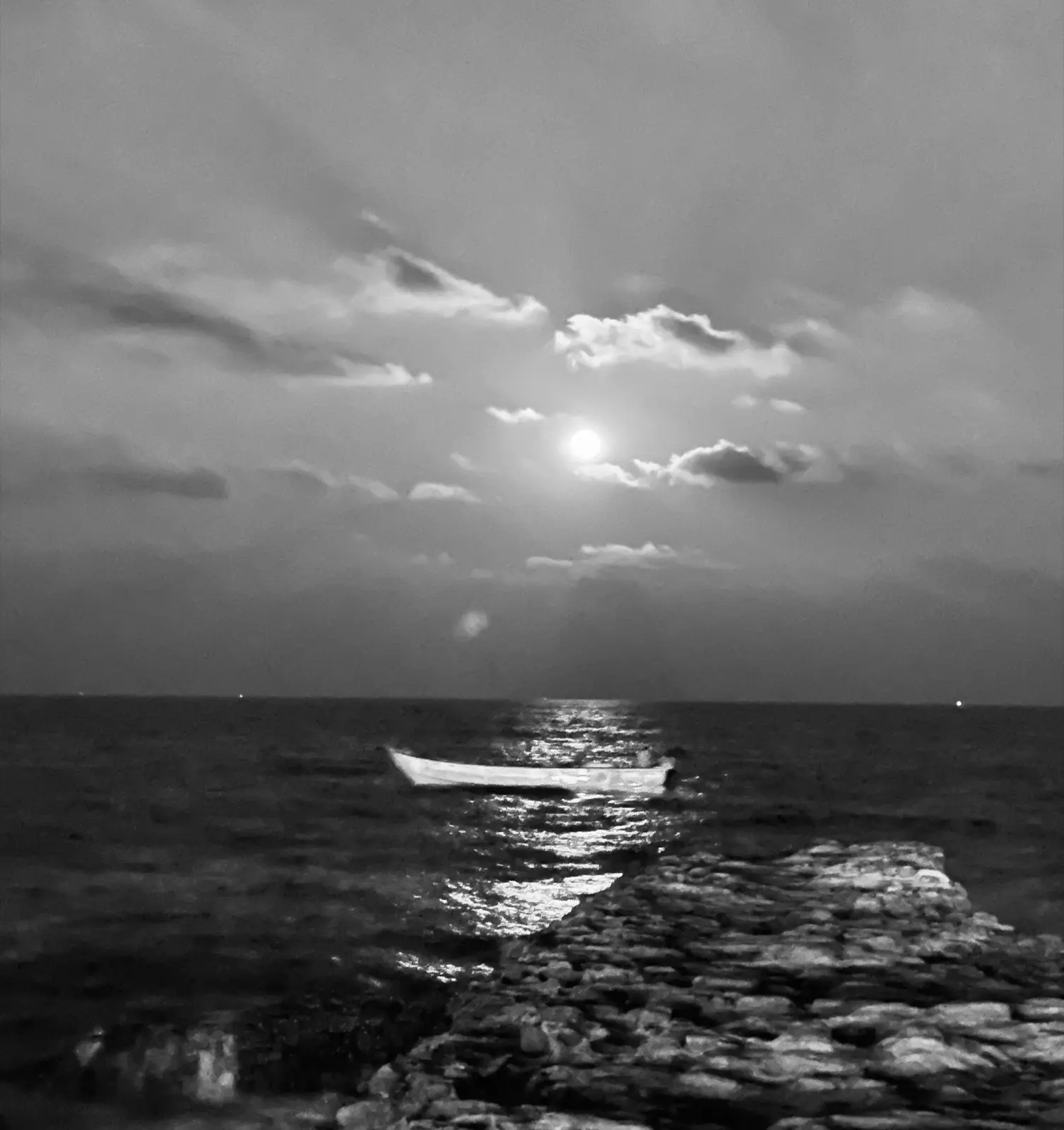 An empty boat adrift on the sea beneath a full moon, its light reflected across the water.