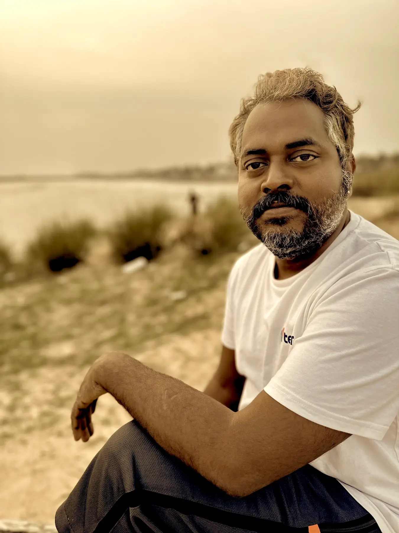 Shankardevy seated outdoors near water.